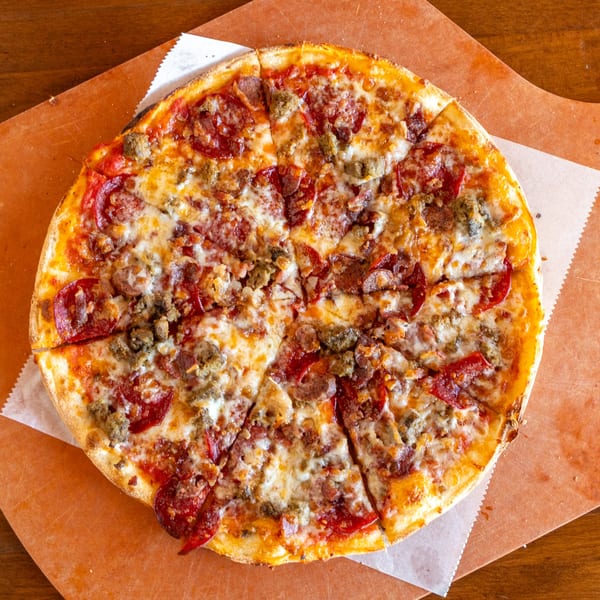 A Stone Hot Pizza with pepperoni and sausage, sliced and ready to eat on a wooden board.