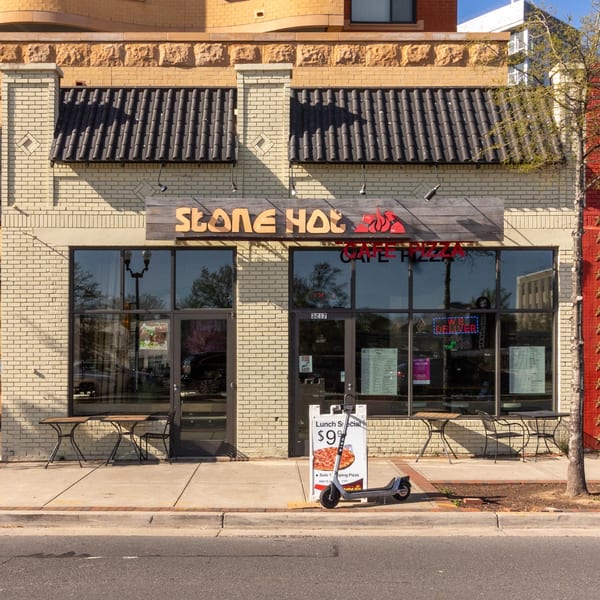 Exterior of Stone Hot Pizza with a lunch special sign and an electric scooter on the sidewalk.
