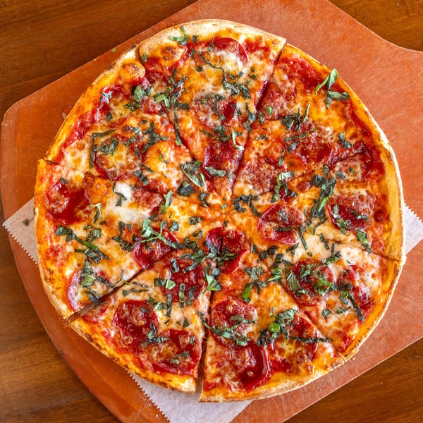 Stone Hot Pizza's pepperoni and basil pizza, sliced and served on a wooden peel.