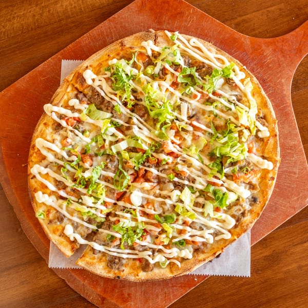 Stone Hot Pizza's taco pizza with ground beef, lettuce, tomatoes, and a creamy drizzle on a wooden peel.