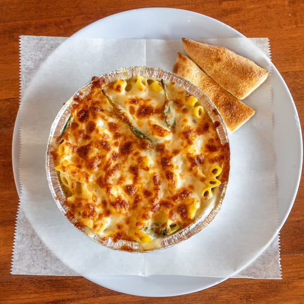 Baked pasta with melted cheese in a foil tin, served with two breadsticks on a white plate.