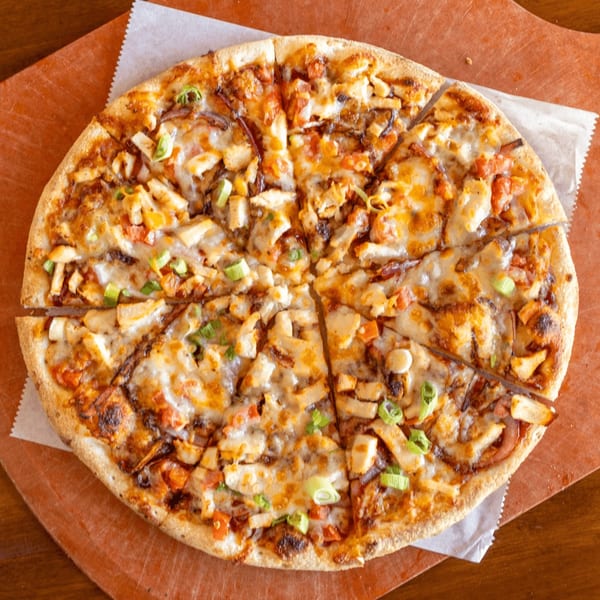 A Stone Hot Pizza with chicken, tomatoes, and green onions, sliced on a wooden board.
