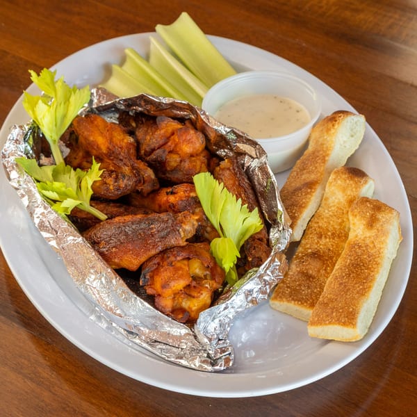 Stone Hot Pizza's chicken wings in foil with celery sticks, dipping sauce, and breadsticks.