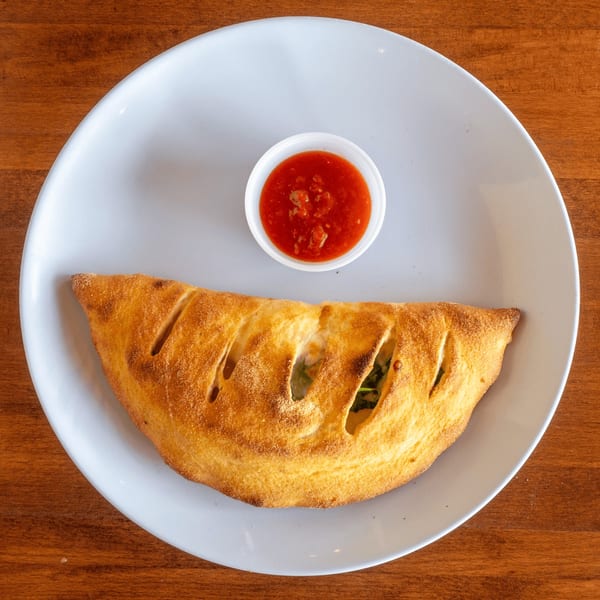 Golden-brown calzone with visible filling and a side of red marinara sauce on a white plate.