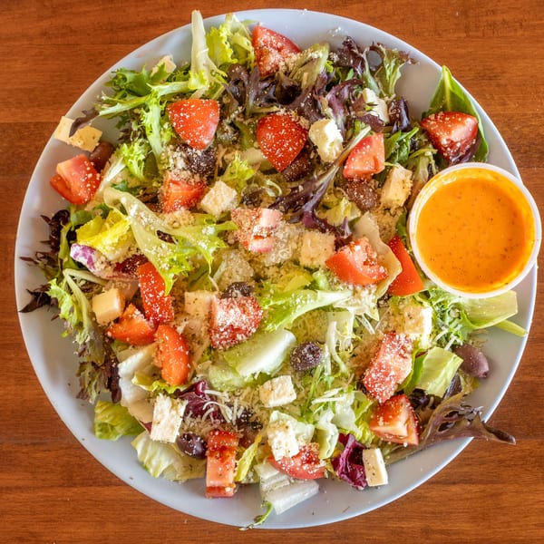 Fresh garden salad with lettuce, tomatoes, feta, olives, and a side of dressing.