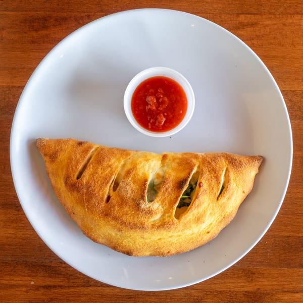 Golden-brown calzone with visible fillings and a side of red marinara sauce on a white plate.
