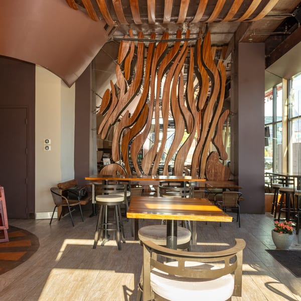 Interior of Stone Hot Pizza with wooden tables, stools, and a large, wavy wooden wall decoration.